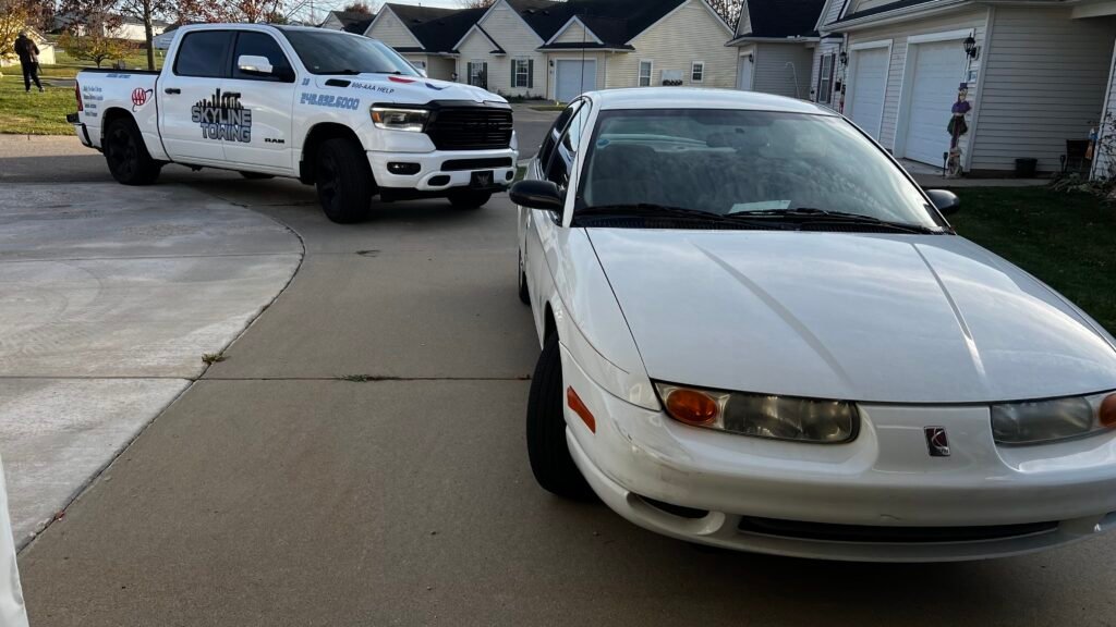 Skyline Towing Ram 1500 roadside service truck in a driveway beside a white Saturn sedan