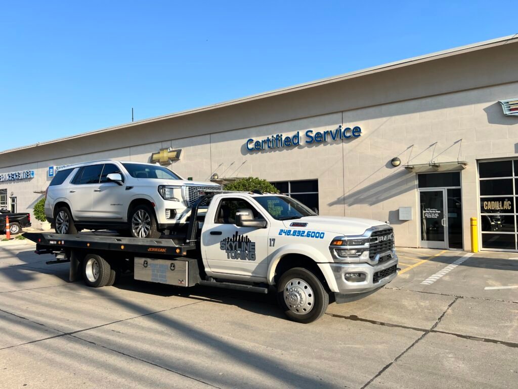 White Skyline Towing Ram 5500 flatbed, truck 17, carrying a white GMC Yukon Denali outside a GM dealership service center