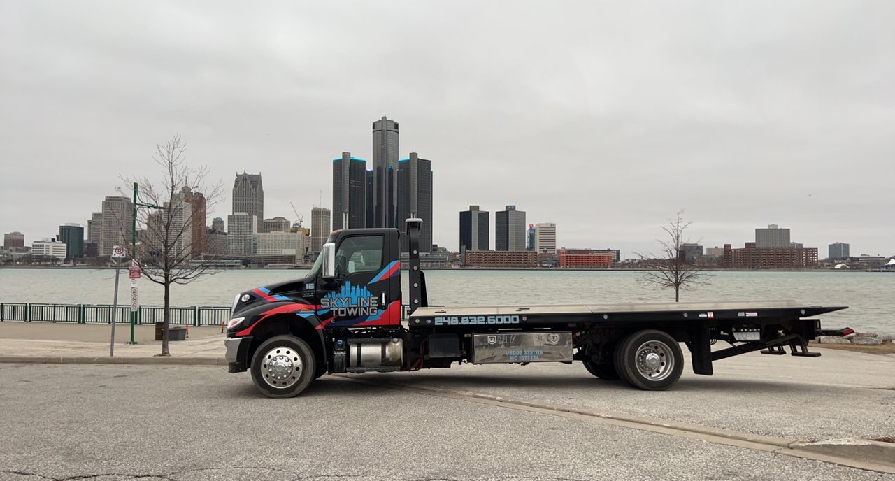 Skyline Towing flatbed on the Detroit riverfront with the downtown skyline behind it